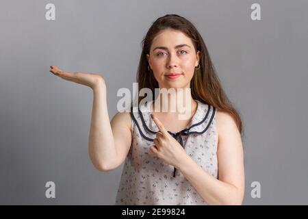 Menschen und Emotionen. Eine junge Brünette in einer Bluse zeigt Hand und Finger zur Seite. Speicherplatz kopieren. Stockfoto