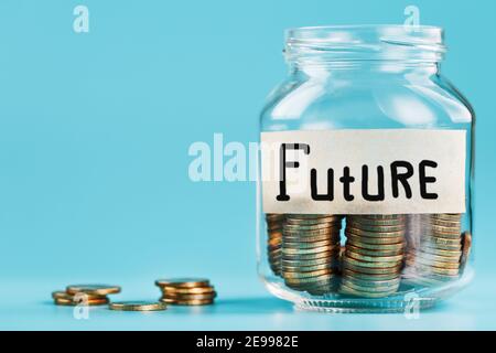 Ein Glas mit Münzen und der Aufschrift ZUKUNFT auf blauem Hintergrund. Budget für Investitionen in die Zukunft, Freiraum Stockfoto