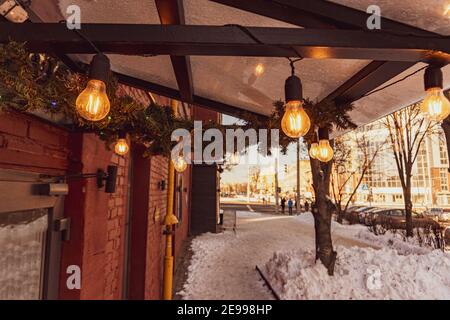 Minsk, Weißrussland - 01. Februar 2021: Das Café Baldachin ist mit Kiefernästen, Edison-Glühbirnen geschmückt und leuchtet mit einem warmen gelben Licht Stockfoto