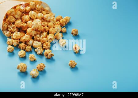 Karamell Popcorn in einem Papierumschlag auf blauem Hintergrund. Köstliches Lob für das Ansehen von Filmen, Serien, Cartoon. Freier Speicherplatz, Nahaufnahme. Minimalis Stockfoto