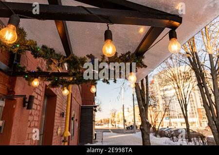 Minsk, Weißrussland - 01. Februar 2021: Der Baldachin des Cafés ist mit Edison-Glühbirnen geschmückt und leuchtet mit einem warmen gelben Licht Stockfoto