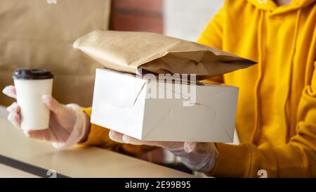 Frau in Handschuhen arbeiten mit Bestellungen zum Mitnehmen. Die Kellner gaben Essen zum Mitnehmen, während die Stadt 19 Lockdown, Coronavirus Herunterfahren kovid. Backen für unterwegs Stockfoto