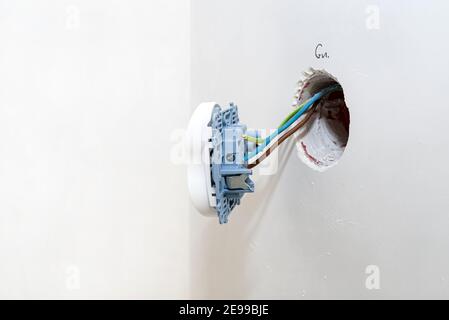 Doppelte Steckdose, die aus der Wand herausragt und an elektrischen Kabeln befestigt ist. Stockfoto