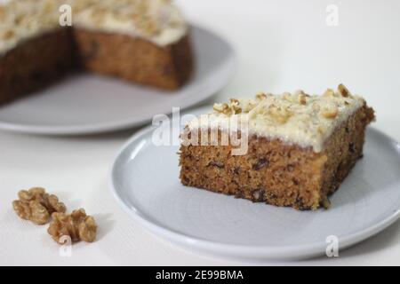 Karotte Walnusskuchen Scheibe mit einer dünnen Schicht von Butter, Zucker und zerkleinerten Walnüssen gekrönt. Fotografiert mit Karotten auf weißem Hintergrund Stockfoto