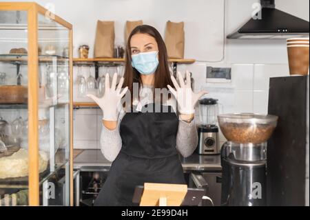 Eine Kellnerin mit Schutzmaske zeigt bei der Kamera ihre Hände in Gummihandschuhen, Sicherheitsmaßnahmen bei Viruserkrankungen, Coronavirus-Pandemie Stockfoto