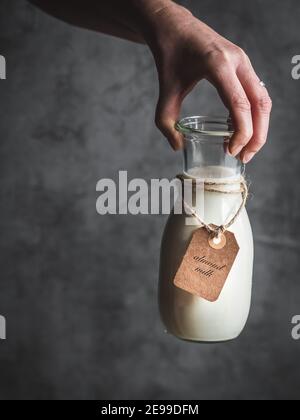 Weibliche Hand hält Flasche Mandelmilch mit Papier-Etikett. Dunkel und launisch. Speicherplatz kopieren. Stockfoto