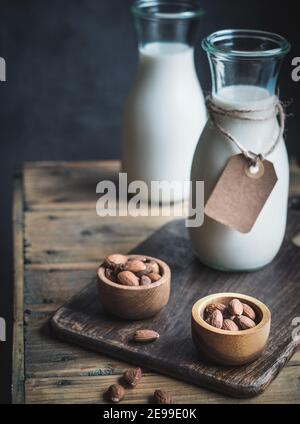 Zwei Flaschen Mandelmilch mit leerem Papieretikett. Holzschalen mit Mandeln auf rustikalem Holztisch. Dunkel und launisch. Speicherplatz kopieren. Stockfoto