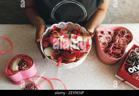 Die Hände einer Frau halten eine Vase mit bunten herzförmigen Keksen in Nahaufnahme. Geschenke zum Valentinstag Stockfoto