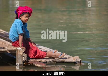 Inle Lake, Myanmar - Dezember 2019: Mädchen sitzt am Flussufer Stockfoto