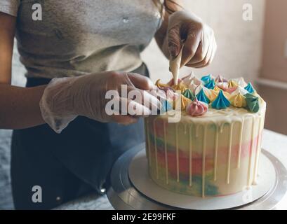 Ein Konditor macht mit eigenen Händen einen Hochzeitstorte und setzt bunte Dekorationen mit Sahne auf die Kuchen. Vorbereitung auf die Feier Stockfoto