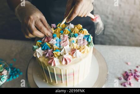 Ein Konditor macht mit eigenen Händen einen Hochzeitstorte und setzt bunte Dekorationen mit Sahne auf die Kuchen. Vorbereitung auf die Feier Stockfoto