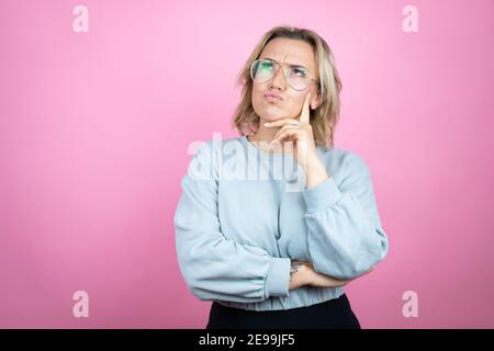 Junge kaukasische Frau trägt Sweatshirt über rosa Hintergrund ernstes Gesicht denken über Frage mit der Hand auf dem Kinn, nachdenklich über verwirrende Idee Stockfoto