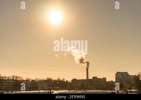 Stadtbild bei Sonnenuntergang. Aus dem Heizraum Rohr geht weißer Dampf, Rauch in den Himmel. Industriegebiet in der Großstadt. Heizung im Winter Stockfoto