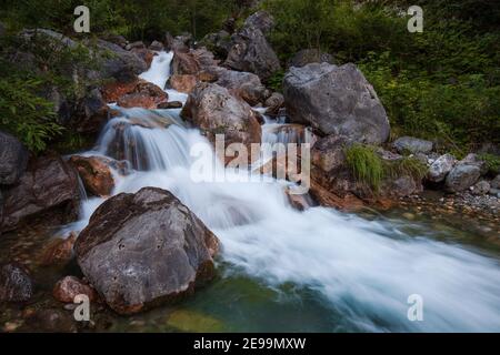 Ein wunderschöner Gebirgsbach aus den Karnischen Alpen mit eisig klarem blaugrünem Wasser umgeben von großen Felsen. Stockfoto