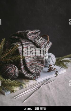 Ein Paar handgestrickte Socken mit Garnkugeln und Stricknadeln. Natürliche Farben. Dunkler rustikaler Hintergrund. Stockfoto