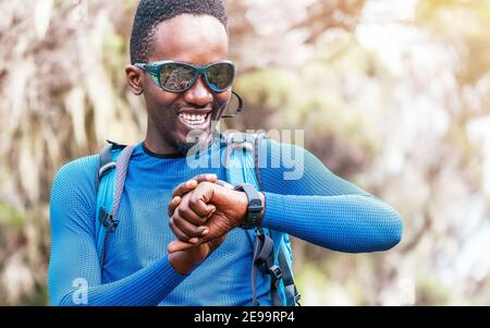 Porträt eines fröhlich lächelnden afroamerikanischen Ethnizität jungen Mannes Überprüfung Eine Herzfrequenz oder Distanz auf der Smartwatch am Handgelenk im Wald Während eines Hiki Stockfoto