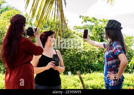 Drei Erwachsene kubanische Fotografinnen aus verschiedenen Generationen nehmen Bilder im Freien zusammen, einer von ihnen macht ein Selfie Stockfoto