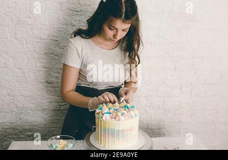 Ein Konditor macht mit eigenen Händen einen Hochzeitstorte und setzt bunte Dekorationen mit Sahne auf die Kuchen. Vorbereitung auf die Feier Stockfoto