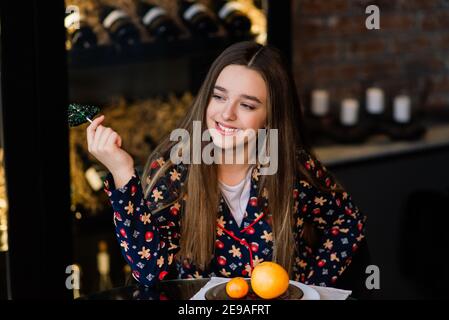 Freundinnen feiern Silvester und Weihnachten und essen Mandarinen auf dem Bett. Es gibt Geschenke und verzierte Tannenzweige mit goldenen Kugeln. Stockfoto