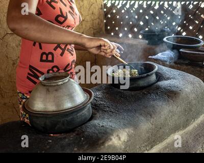 HIRIWADUNNA, SRI LANKA - 10. März 2019: Junge südasiatische Frau kocht Reis und Curry in der traditionellen ländlichen Outdoor-Küche. Stockfoto