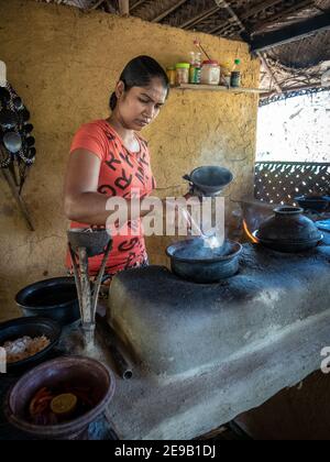 HIRIWADUNNA, SRI LANKA - 10. März 2019: Junge südasiatische Frau kocht Reis und Curry in der traditionellen ländlichen Outdoor-Küche. Stockfoto