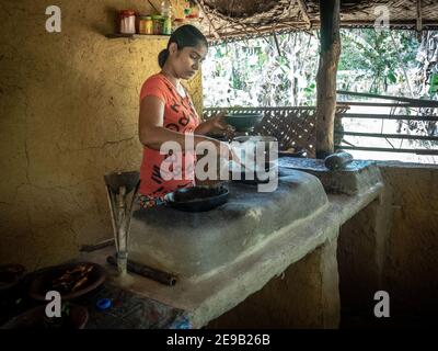 HIRIWADUNNA, SRI LANKA - 10. März 2019: Junge südasiatische Frau kocht Reis und Curry in der traditionellen ländlichen Outdoor-Küche. Öko-Dorf Hiriwadunna. Stockfoto