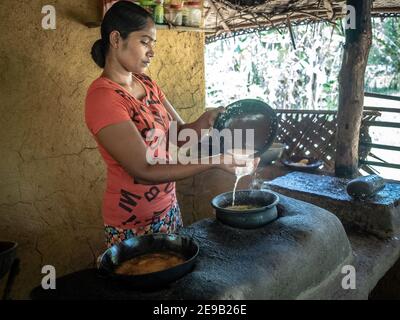 HIRIWADUNNA, SRI LANKA - 10. März 2019: Junge südasiatische Frau kocht Reis und Curry in der traditionellen ländlichen Outdoor-Küche. Öko-Dorf Hiriwadunna. Stockfoto