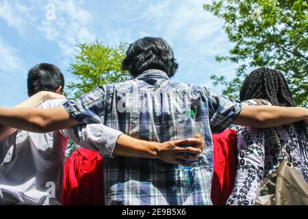 Freunde der Absolventen - Rückansicht der Gruppe von Multiethnische Freunde mit Armen um die Schultern - eins Snacks halten - im Gespräch mit Graduat Stockfoto