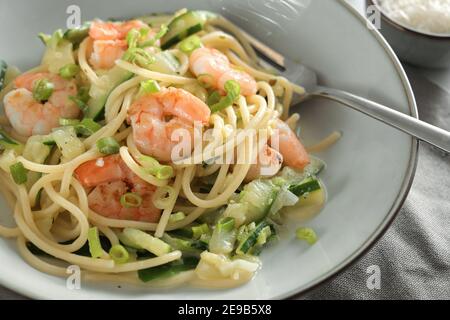 Spaghetti mit Garnelen, Zucchini und Frühlingszwiebeln in einem grauen Teller mit Gabel, Nahaufnahme einer gesunden mediterranen Mahlzeit, ausgewählter Fokus, schmal Stockfoto