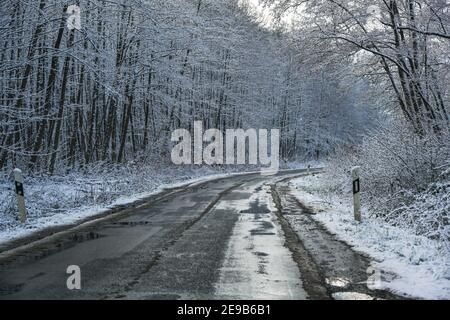 Landstraße durch einen Wald im Winter, Gefahr auf dem rutschigen nassen und eiskalten Asphalt, Verkehrs- und Transportkonzept, Kopierraum, ausgewählter FOC Stockfoto
