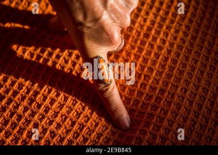 Weibliche Hand mit einem orangefarbenen Ring auf einem orangefarbenen Deckel Stockfoto