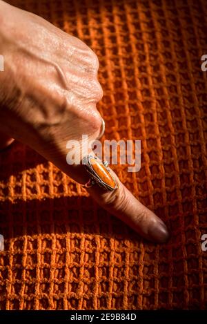 Weibliche Hand mit einem orangefarbenen Ring auf einem orangefarbenen Deckel Stockfoto