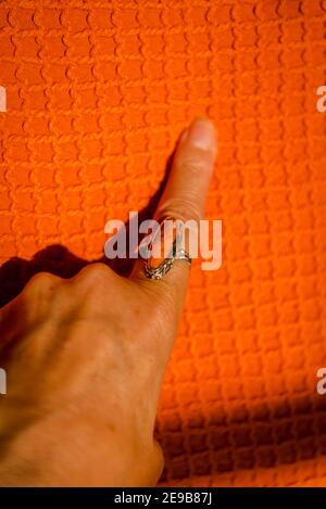 Weibliche Hand mit einem orangefarbenen Ring auf einem orangefarbenen Deckel Stockfoto