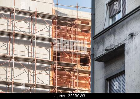 Nahaufnahme auf der Baustelle einer Wand von Ein Wohnhaus aus rotem Backstein in einer Stadt Erneuerungsbetrieb mit Gerüsten und einem älteren BU Stockfoto