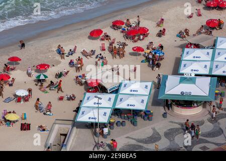 Am späten Nachmittag entspannen sich die Menschen unter Sonnenschirmen am Strand von Copacabana in Rio de Janeiro in Brasilien. Der Strand liegt am Atlantik. Stockfoto