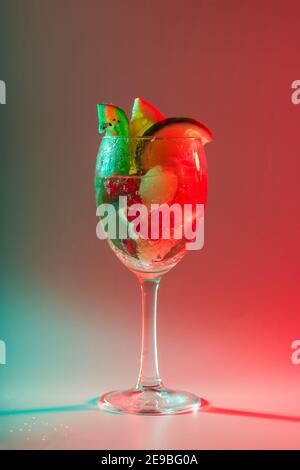 Heller Cocktail mit frischen Früchten in einem Glas mit mehrfarbigem Neonlicht. Alkoholische, alkoholfreie Getränke, Unterhaltung, Partys, Nachtclub. Stockfoto