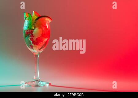 Heller Cocktail mit frischen Früchten in einem Glas mit mehrfarbigem Neonlicht. Alkoholische, alkoholfreie Getränke, Unterhaltung, Partys, Nachtclub. Stockfoto