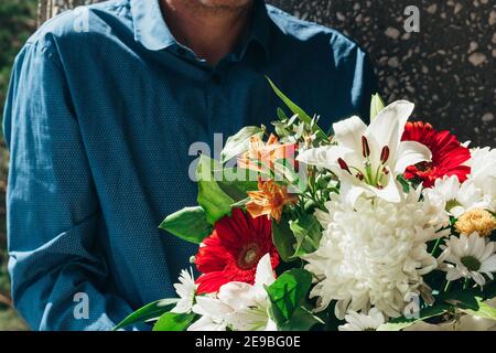 Ein Mann mittleren Alters in blauem Hemd mit hellen Bouquet von frischen bunten gemischten Blumen. Ein romantisches Geschenk für geliebte Frau für jeden Anlass. Nahaufnahme. Stockfoto