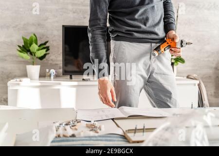 Mittelteil des Mannes zusammen Selbstmontage Möbel zu Hause Halten Sie den elektrischen Schraubendreher nach den Anweisungen - halbe Länge vorne DIY anzeigen Stockfoto