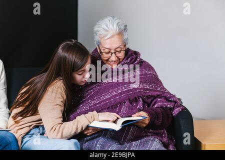 Lateinische Enkelin und mexikanische Großmutter lesen ein Buch und Tablet In Mexiko-Stadt Stockfoto