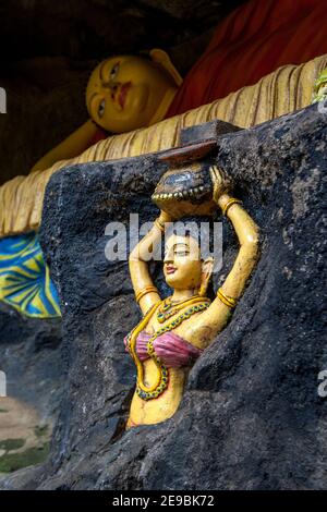 Eine liegende Buddha-Statue mit einer weiblichen Figur, die einen in Fels gehauenen Behälter im Vordergrund auf dem Pfad hält, der zum Adams Peak in Sri Lanka führt. Stockfoto