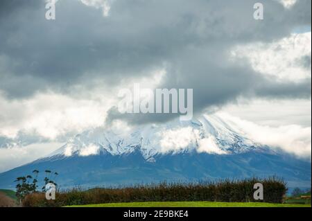 Mount Taranaki (Mount Egmont), Egmont National Park, Neuseeland. Ländliche Landschaft, schneebedeckten Berg unter Regenwolken mit grünem Vordergrund. Stockfoto