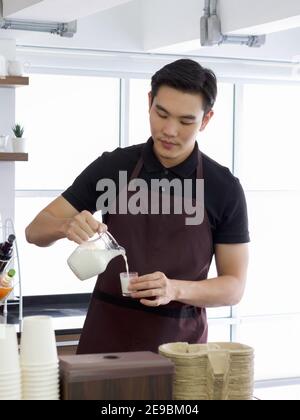 Junger asiatischer Mann gießt Milch in Messbecher. Professioneller Barista, der Kaffee auf der Theke zubereitet. Stockfoto