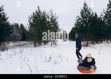 Ein Mann in warmer Winterkleidung rollt Frauen auf einem roten Schlauch. Stockfoto