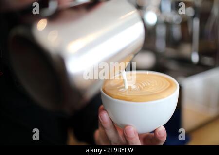 Männliche Hände Gießen Milch und Vorbereitung für Cappuccino-Kaffee Stockfoto