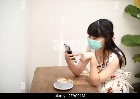 Portrait Weiblich mit Maske mit Smartphone im Café auf covid-19 Virus Ausbruch , Business-Konzept Stockfoto