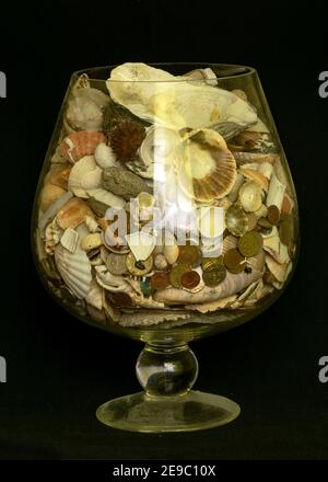 Foto mit einem großen Glasbehälter, einer Vase mit vielen verschiedenen Muscheln und Metallmünzen Stockfoto