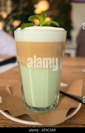 Kaffee am Morgen. Latte mit Milch, Sirup, Schlagsahne. Verziert mit Minzblättern. Ein Glas Kaffee auf einer Untertasse. Nahaufnahme. Stockfoto