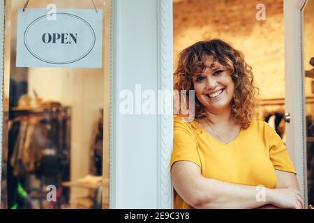 Porträt eines Bekleidungsladens Besitzer stehen an der Tür mit offenem Schild. Attraktive Bekleidungsgeschäft Besitzer steht in ihrem Shop Eingang. Stockfoto