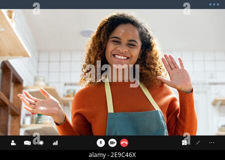 Hübsche afroamerikanische Frau lächelnd und winkende Hände zum Kamera macht Videoanruf in der Küche zu Hause Stockfoto